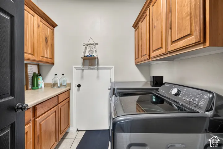 Dedicated laundry room featuring rich wood cabinetry, white appliances including a refrigerator and top-load washer, tile flooring, and ample storage with upper and lower cabinetry throughout