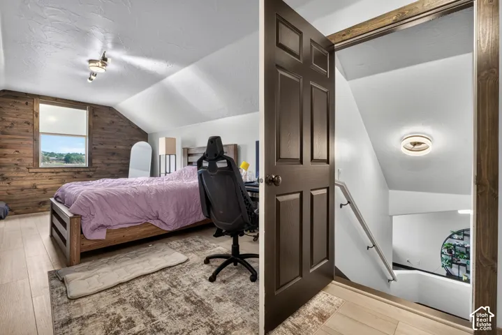 Attic bedroom featuring sloped ceilings with recessed lighting, wood-finish flooring, and a brick accent wall with a window