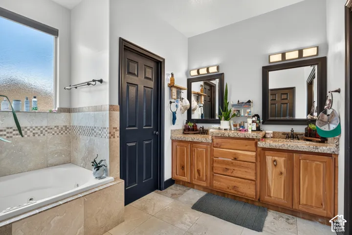 Spa-inspired primary bathroom featuring dual wood-finish vanities with granite countertops, framed mirrors with integrated lighting, a soaking tub with tile surround, and a separate walk-in shower