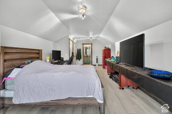 Spacious primary suite featuring vaulted ceilings with skylights, wood-finish flooring throughout, and a wood-frame bed with upholstered headboard