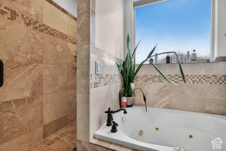 Spa-inspired master bath featuring a soaking tub with brass accents, dual-control matte black faucetry, and a spacious walk-in shower with large-format travertine tile surround