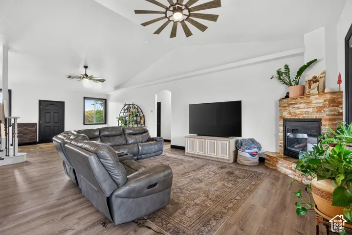 Spacious living room featuring vaulted ceilings with exposed beam detailing, wide-plank wood-finish flooring, and a brick fireplace with built-in cabinetry