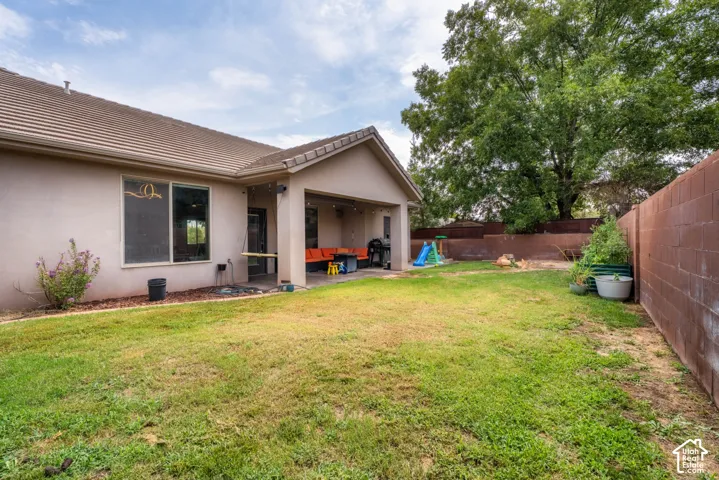 Spacious backyard with mature landscaping and established trees, brick perimeter fencing, and a covered patio extension adjoining the single-story residence