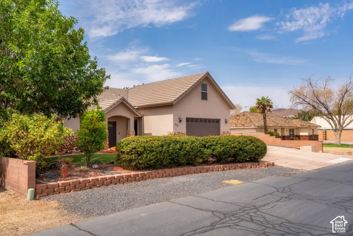 Charming single-story residence featuring a warm stucco exterior with a pitched tile roof, brick entry columns, and a two-car garage