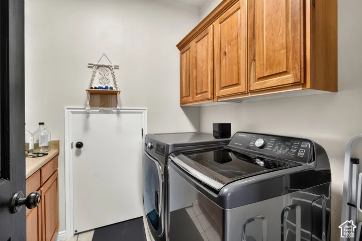 Dedicated laundry room featuring stacked washer and dryer with modern black finish, wood cabinetry above, white front-load refrigerator, and dark tile flooring