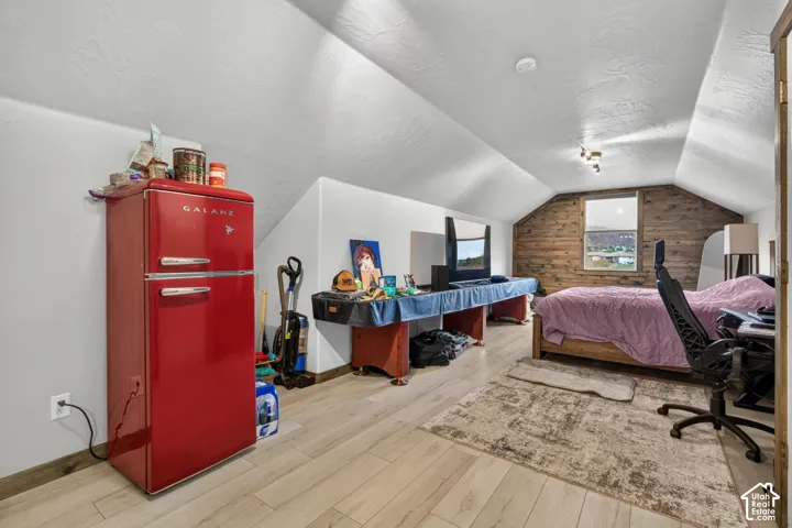 Versatile attic space with vaulted ceilings, wood-finish flooring, and exposed brick accent wall