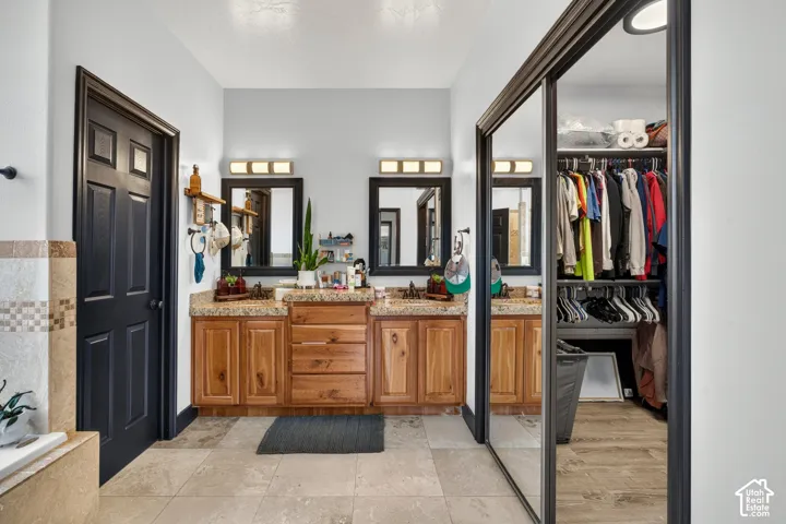 Dual vanity with granite countertops, wood-finish cabinetry, tile flooring, and a mirrored closet