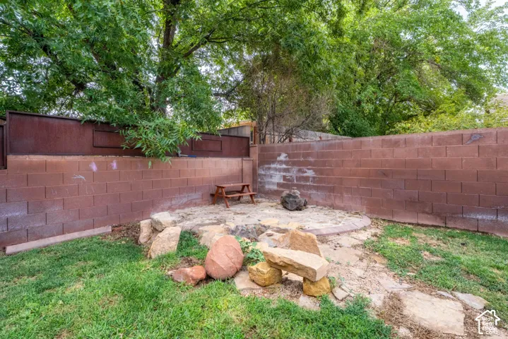 Private backyard retreat featuring a brick perimeter wall, mature shade trees, and a circular fire pit area surrounded by natural stone seating