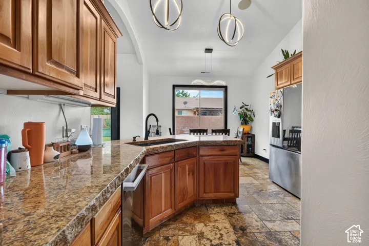 Kitchen featuring granite countertops, wood cabinetry, stainless steel refrigerator, and modern pendant lighting