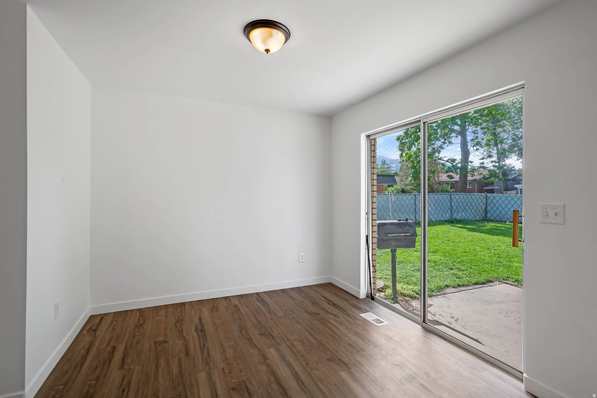 Wood-finish flooring, white walls, ceiling-mounted light fixture, sliding glass door, and a private patio