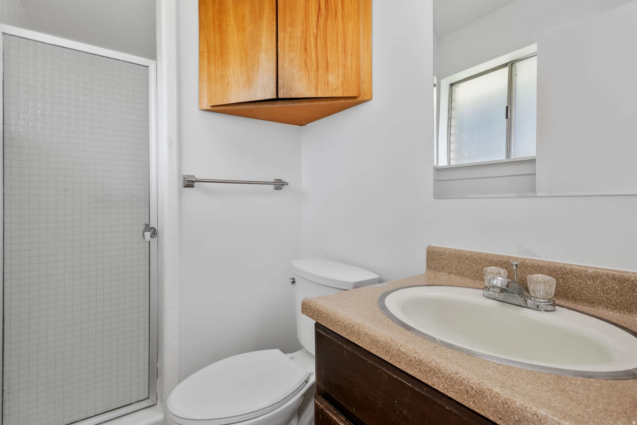 White tiled shower enclosure, corner wood-finish cabinetry, integrated vanity sink, and a mirrored wall