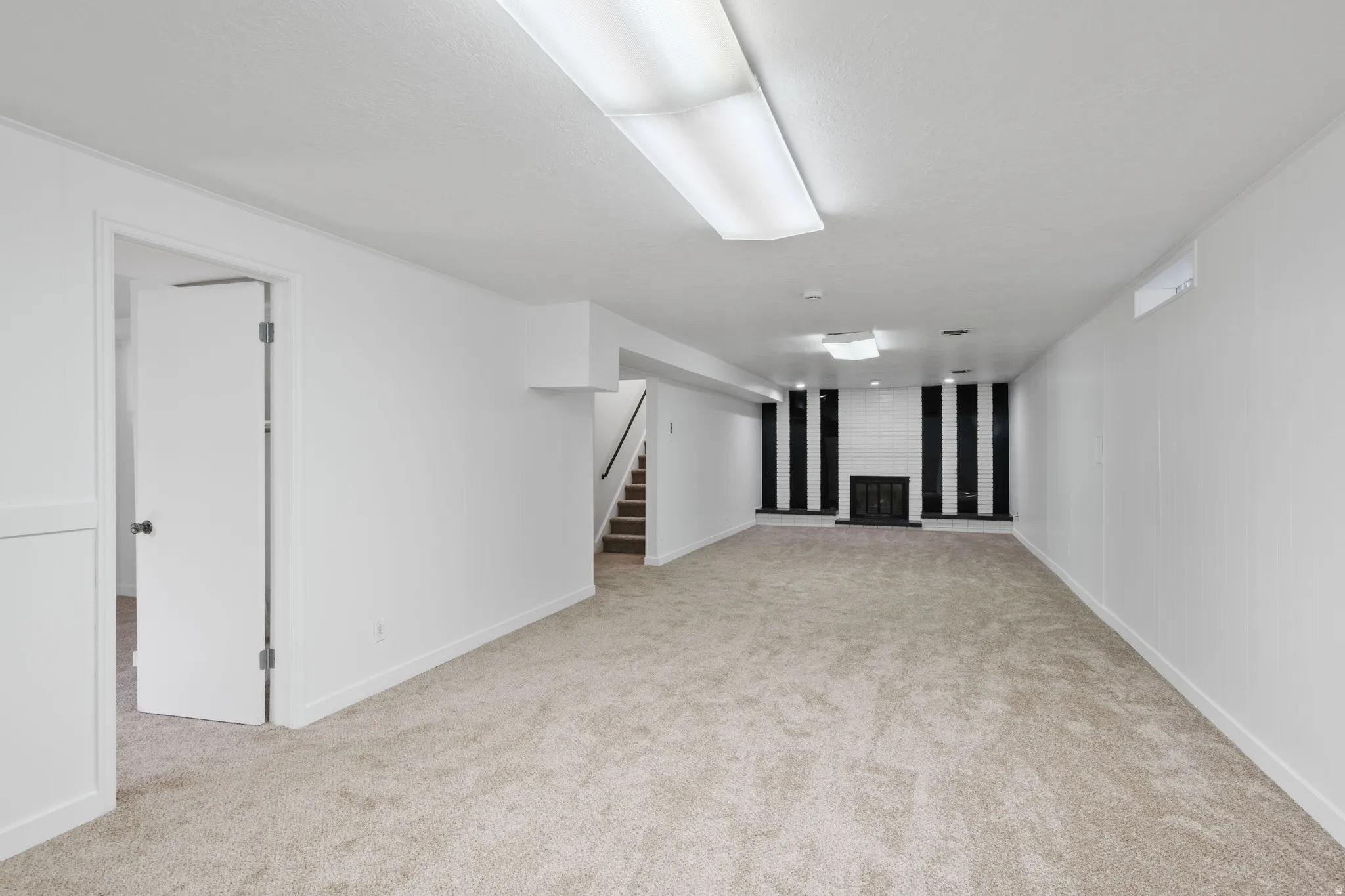 Expansive carpeted room featuring a fireplace with a black and white tiled surround and a black metal grate