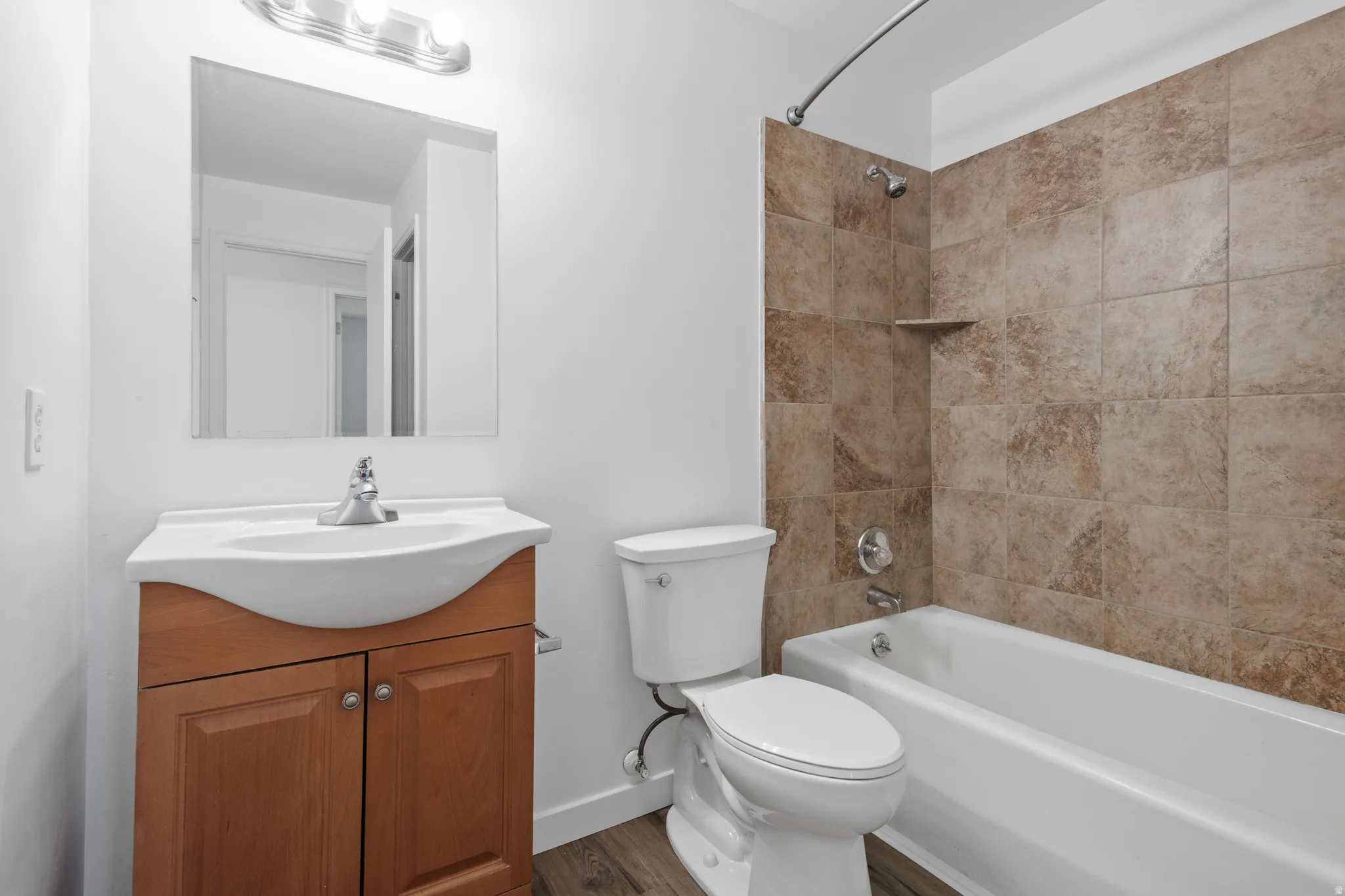 Bathroom featuring a wood-finish vanity with an integrated sink, a large wall mirror, and a full-size bathtub with tiled surround