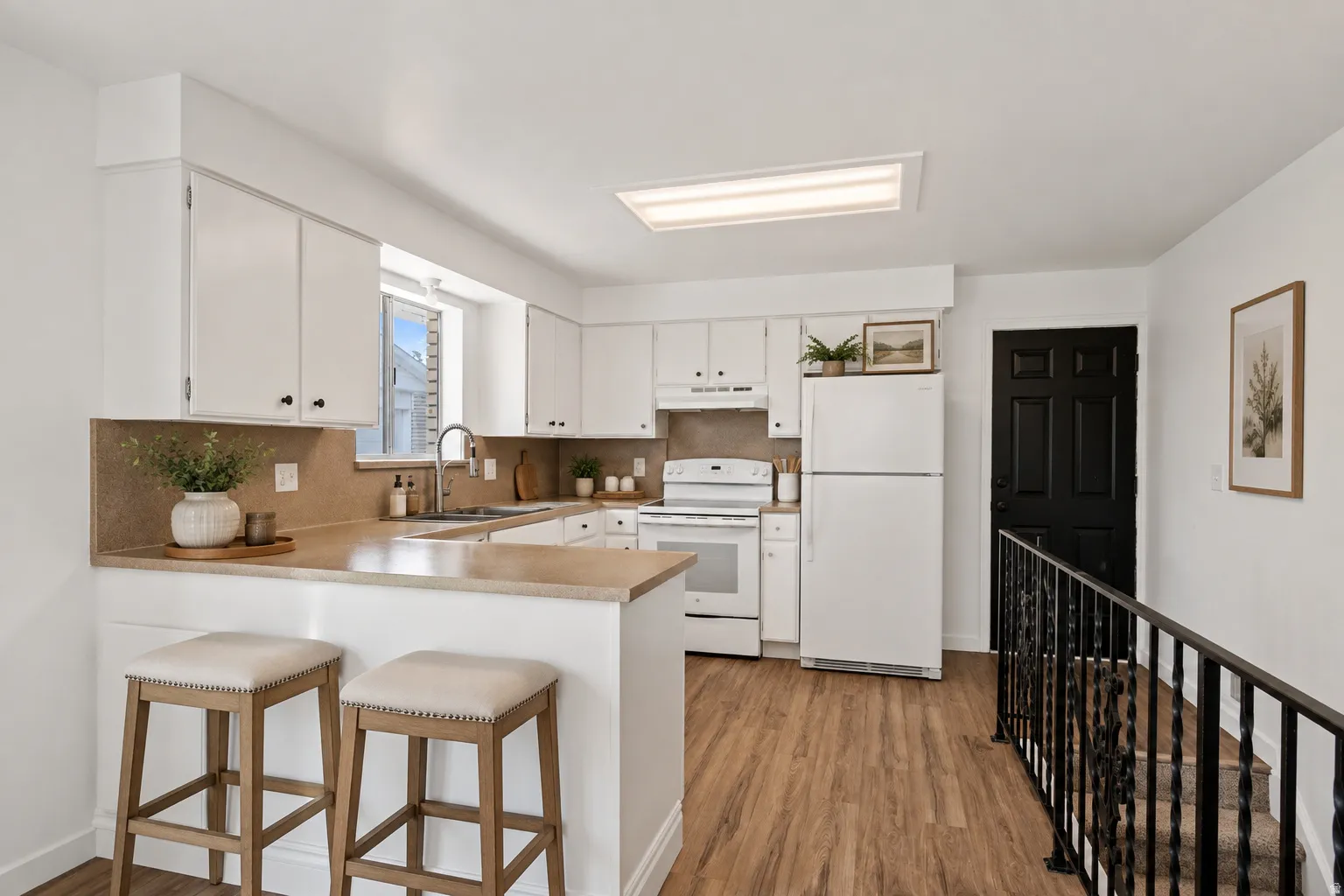 Kitchen featuring white cabinetry, light-toned countertops, a stainless steel sink with a gooseneck faucet, and wood-finish flooring