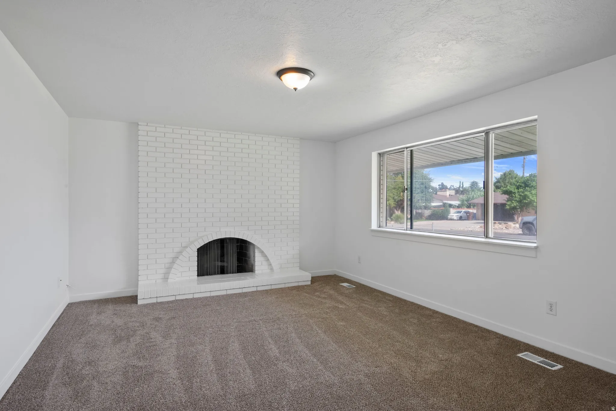 Painted brick fireplace with an arched firebox, neutral carpet flooring, and a large window