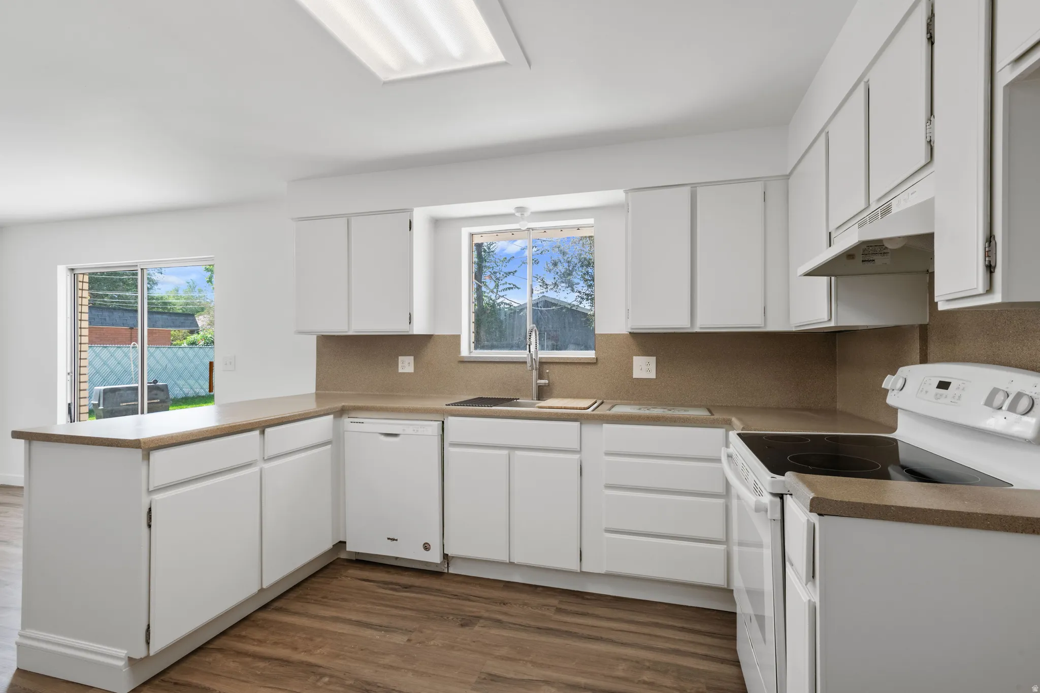 Kitchen featuring wood-finish flooring, white cabinetry, a built-in dishwasher, and a white electric range with an overhead exhaust hood