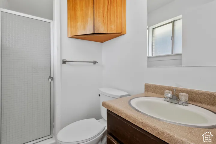 White tiled shower enclosure, corner wood-finish cabinetry, integrated vanity sink, and a mirrored wall