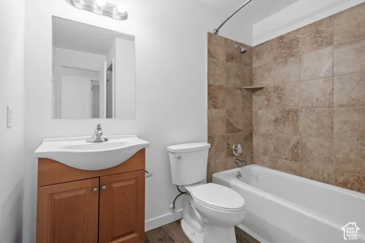 Bathroom featuring a wood-finish vanity with an integrated sink, a large wall mirror, and a full-size bathtub with tiled surround