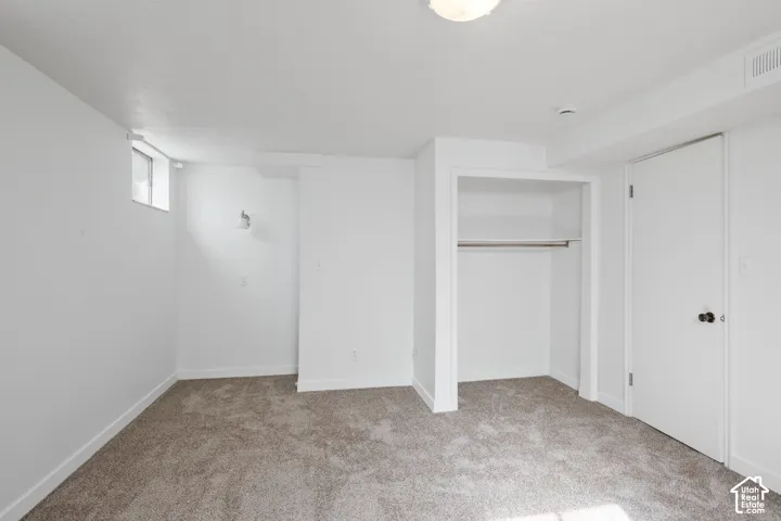 Neutral-toned carpeting, white painted walls, and built-in closet with shelving and hanging rod
