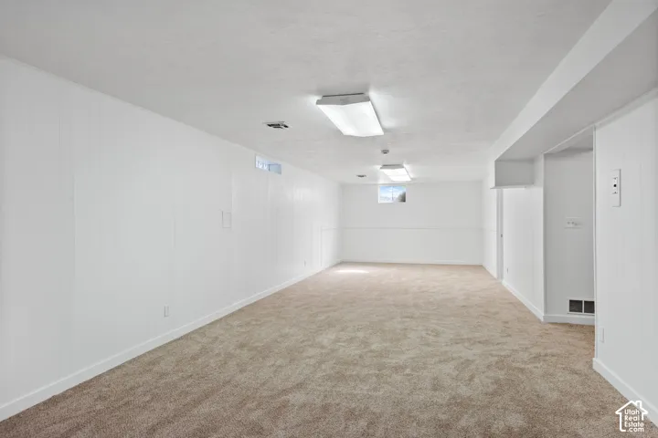 Expansive room featuring neutral-toned carpet, white paneling, white painted ceiling, and overhead fluorescent lighting