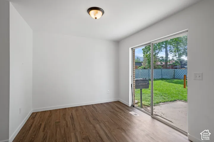 Wood-finish flooring, white walls, ceiling-mounted light fixture, sliding glass door, and a private patio