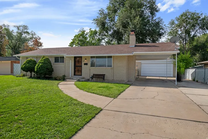 Brick exterior featuring a covered carport, mature front yard landscaping, a paved driveway, and a secure entry door