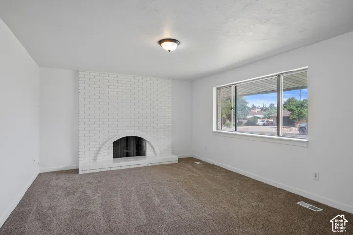 Painted brick fireplace with an arched firebox, neutral carpet flooring, and a large window