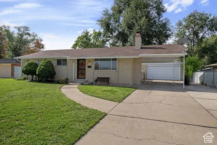 Brick exterior featuring a covered carport, mature front yard landscaping, a paved driveway, and a secure entry door