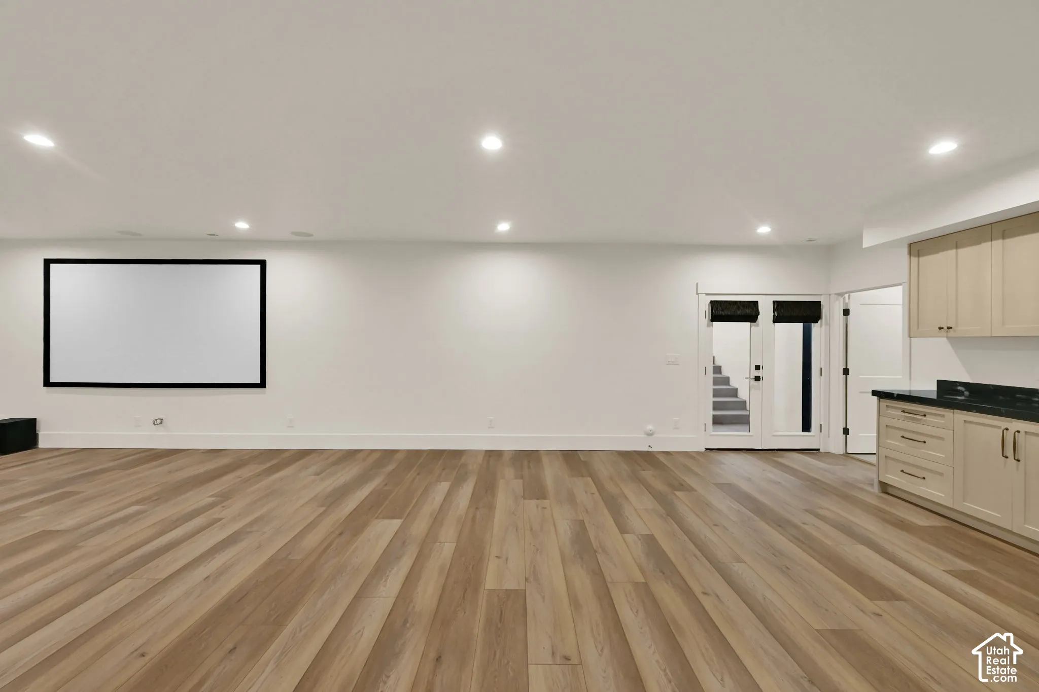 Spacious room featuring wood-finish flooring, recessed lighting, and a large projection screen