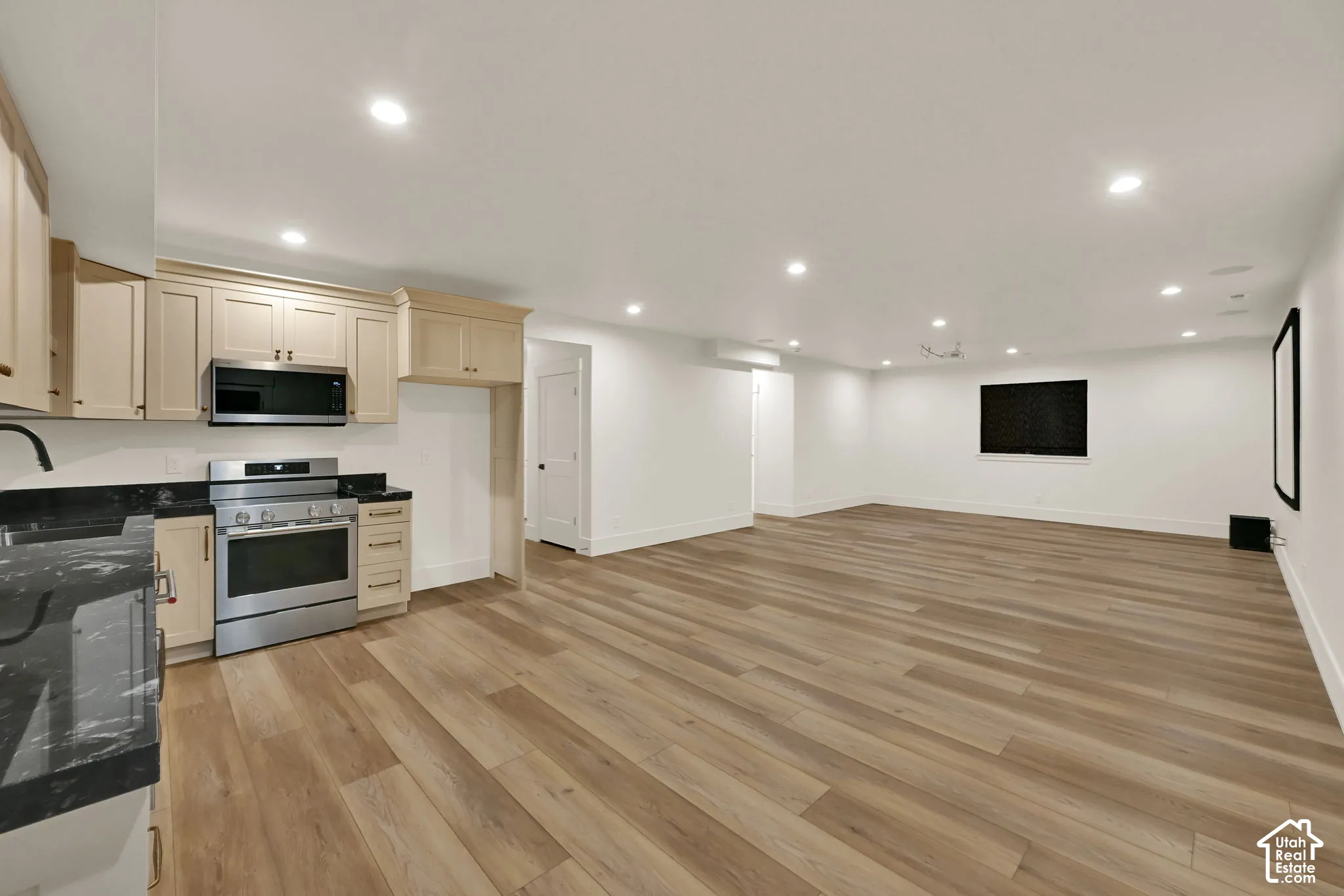 Spacious open-concept area featuring wood-finish flooring, a kitchen area with stainless steel appliances, dark countertops, and light-colored cabinetry