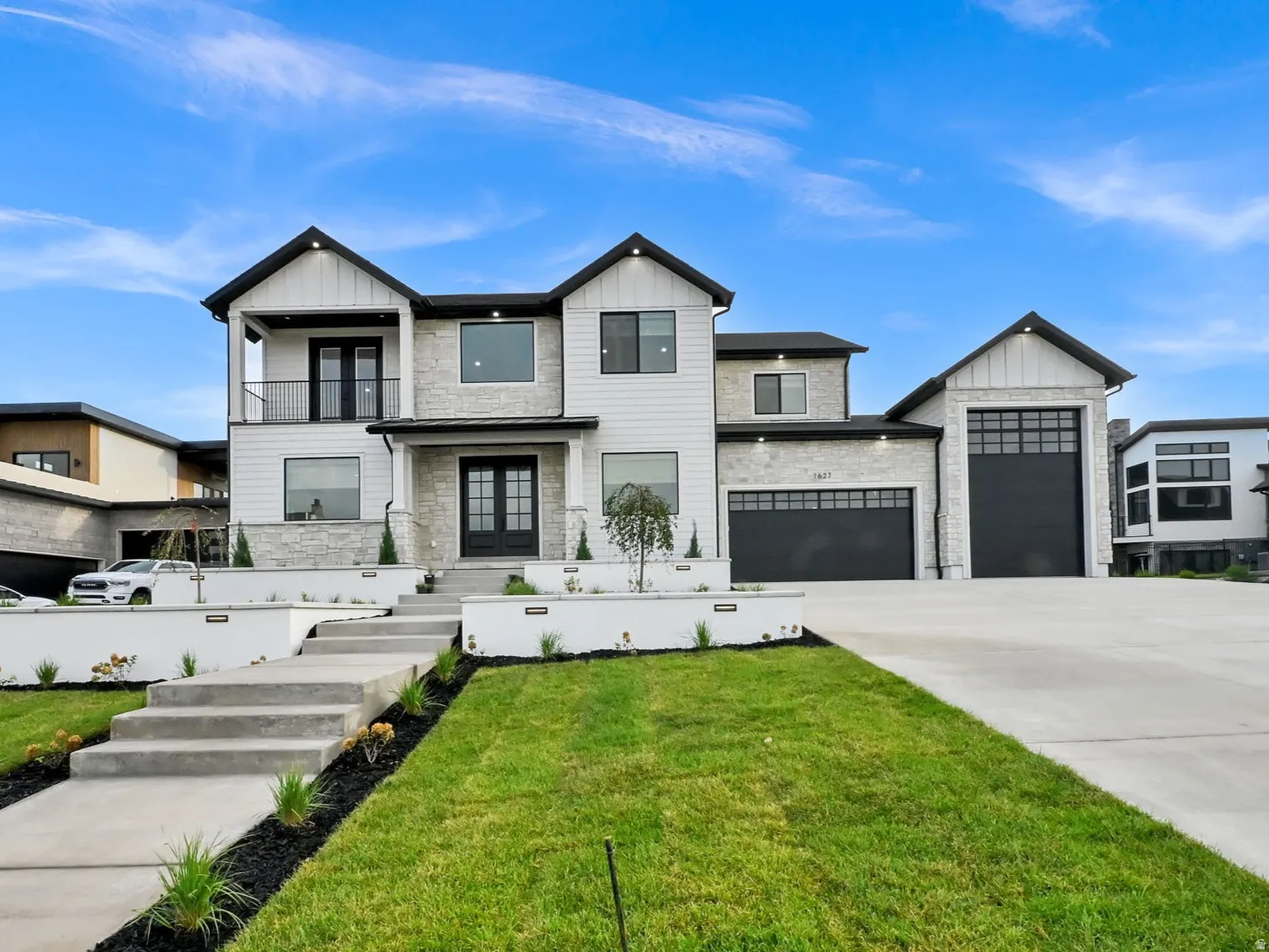 Modern exterior with white siding and stone accents, concrete driveway, attached garage, and a concrete walkway with tiered landscaping