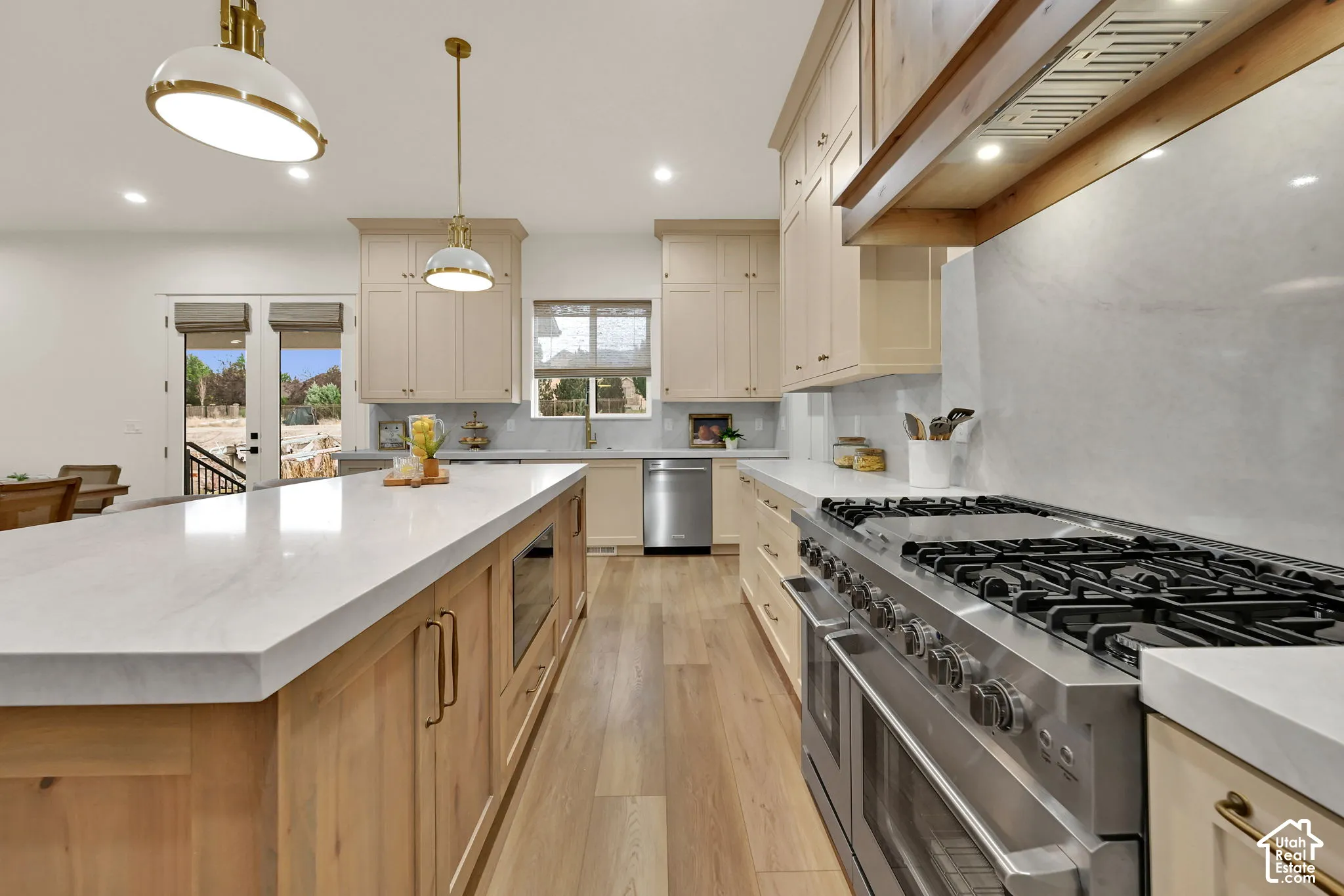 Gourmet kitchen with a large central island, light wood-finish flooring, stainless steel appliances, and cream-colored cabinetry