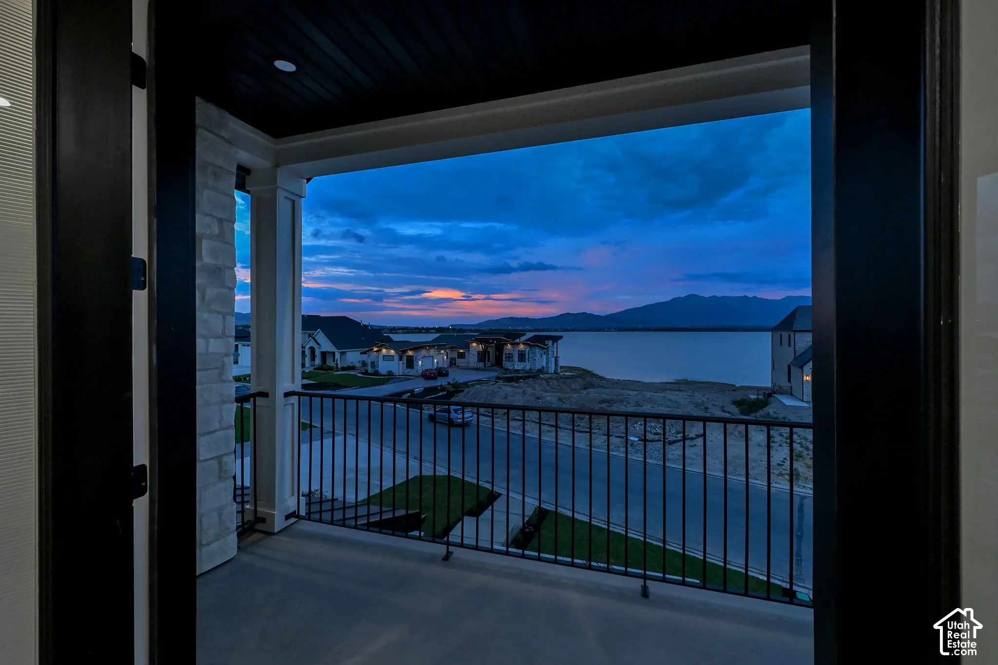 Balcony with concrete flooring and black metal railings, stone columns, and wood-paneled ceiling