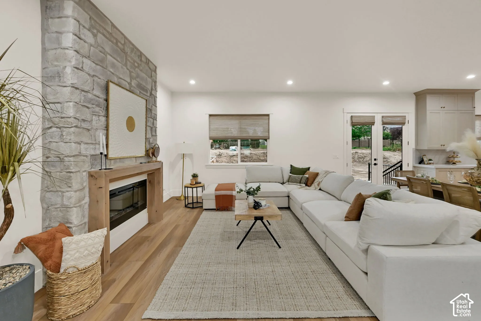 Expansive living area featuring stone-clad fireplace surround, wood-finish flooring, recessed lighting, and double glass panel doors