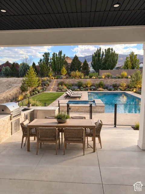Expansive outdoor living area featuring a built-in outdoor kitchen with grill, concrete patio, inground pool, and integrated hot tub
