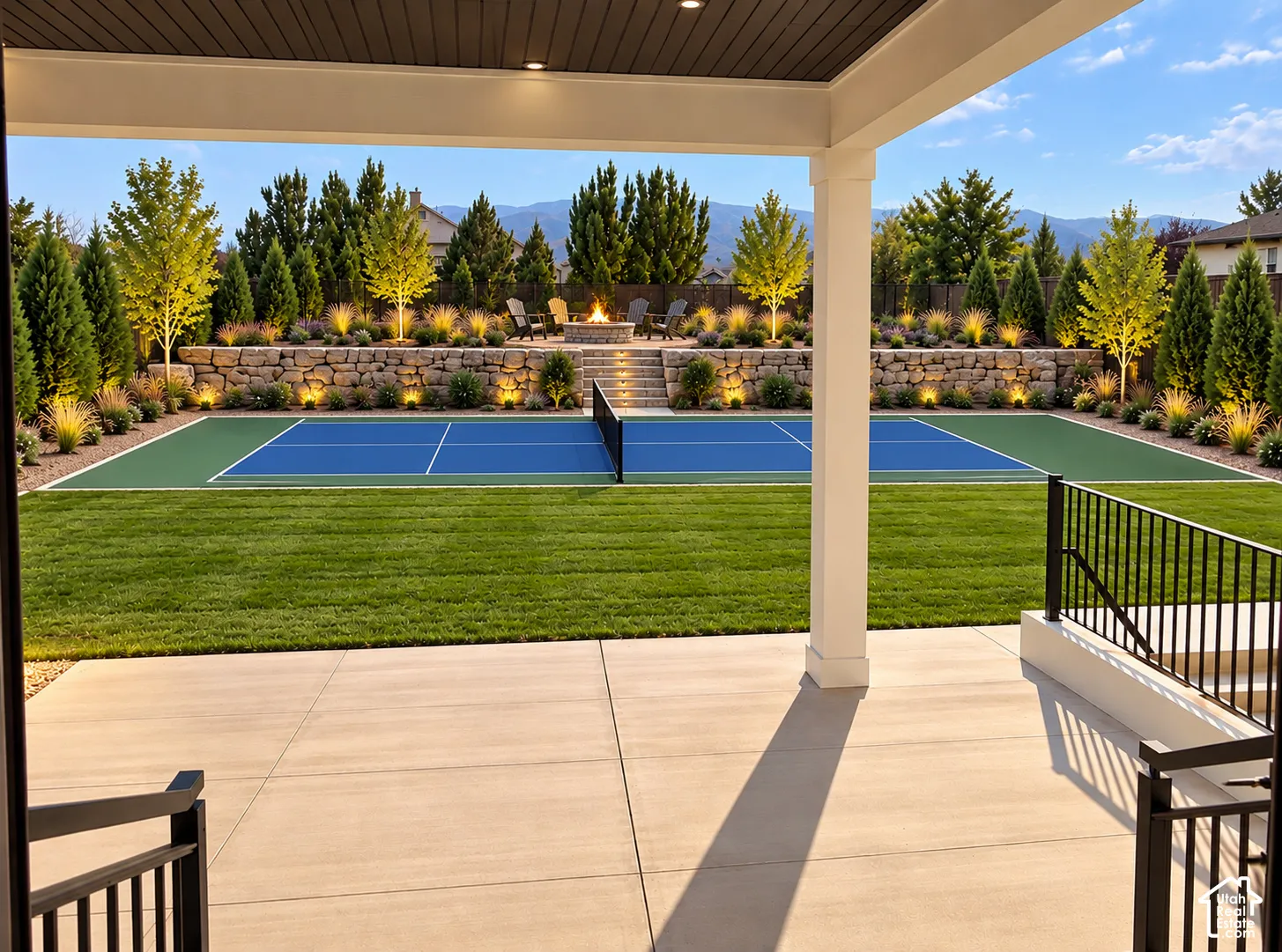Expansive backyard featuring a manicured lawn, a built-in pickleball court, and a multi-tiered stone retaining wall with integrated lighting
