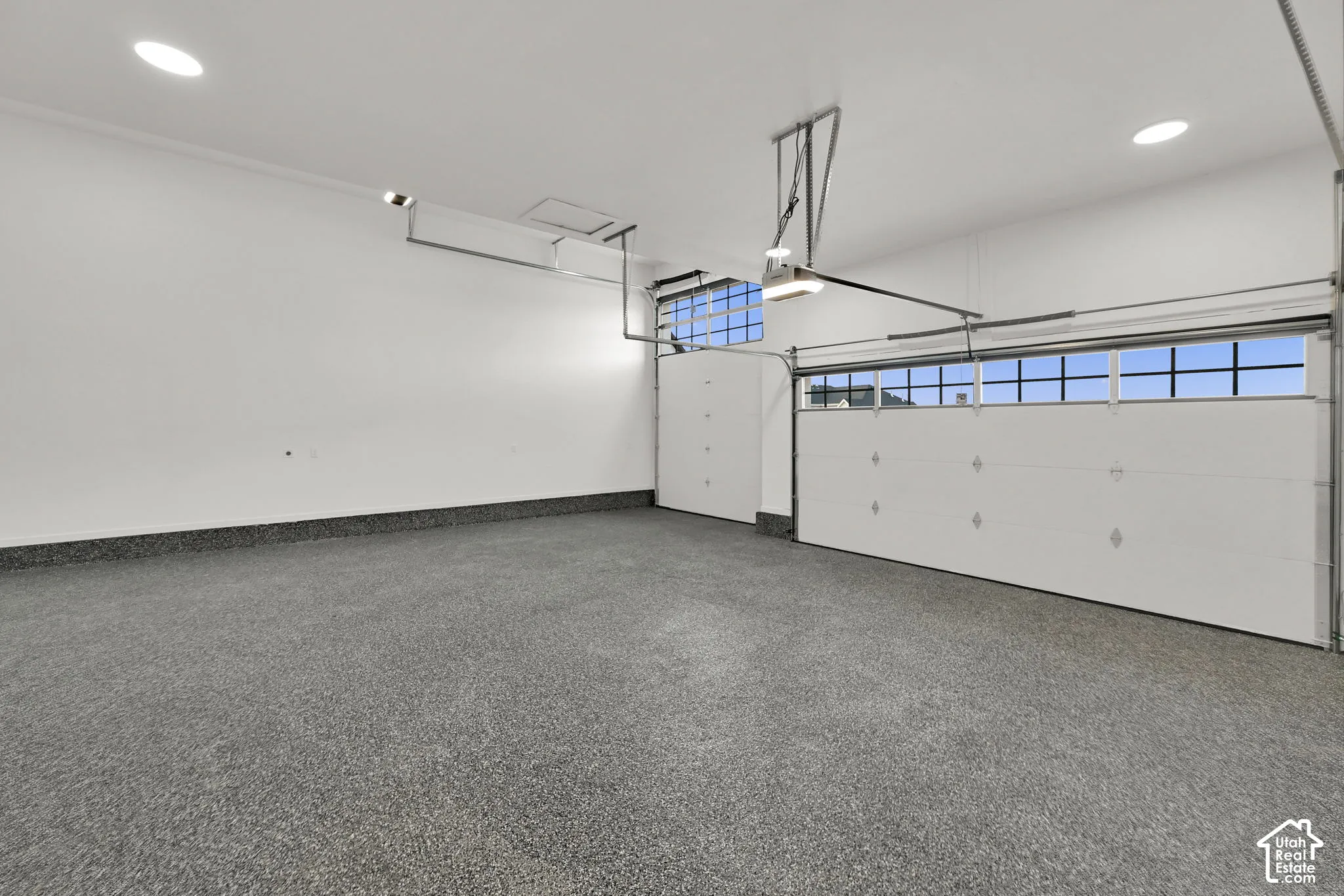 Epoxy-coated flooring, two overhead garage doors with window panels, recessed lighting, and white finished walls
