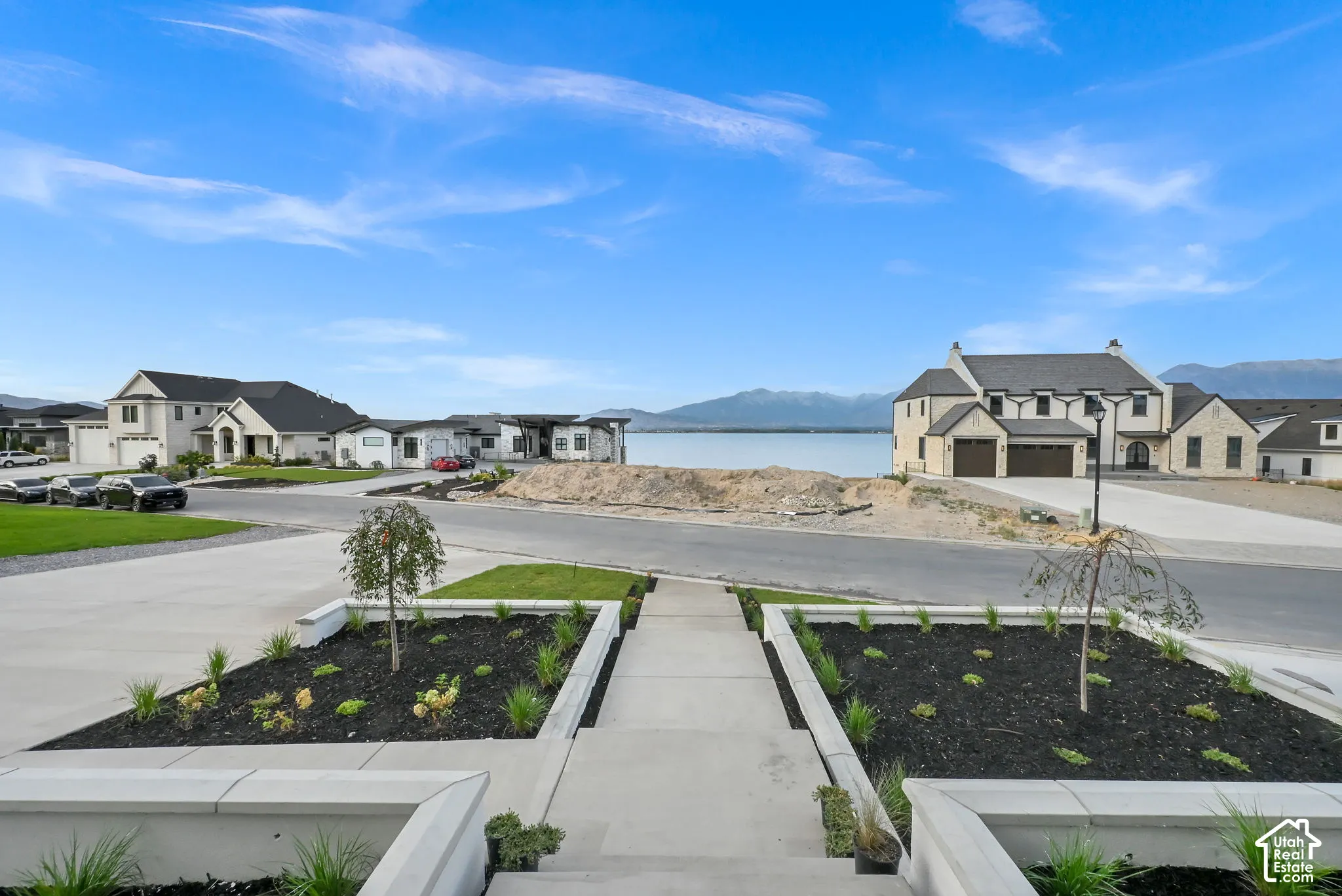 Exterior landscaping featuring a concrete pathway with planted beds, a paved driveway, and a residential street with distant houses