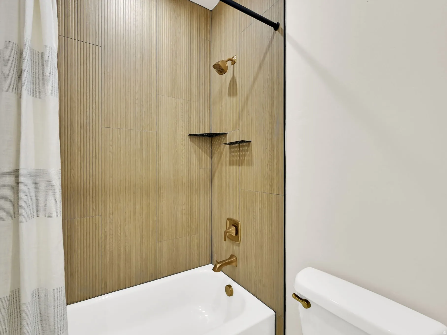 Bathtub with wood-look tile surround, bronze-finish fixtures, and built-in corner shelves
