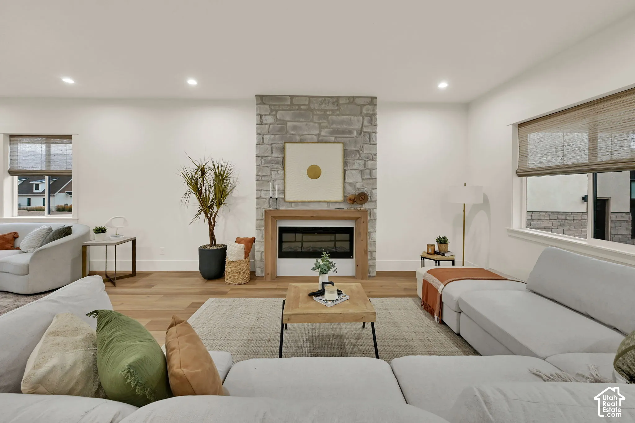 Stone-clad fireplace with wood surround, recessed lighting, wood-finish flooring, and multiple windows