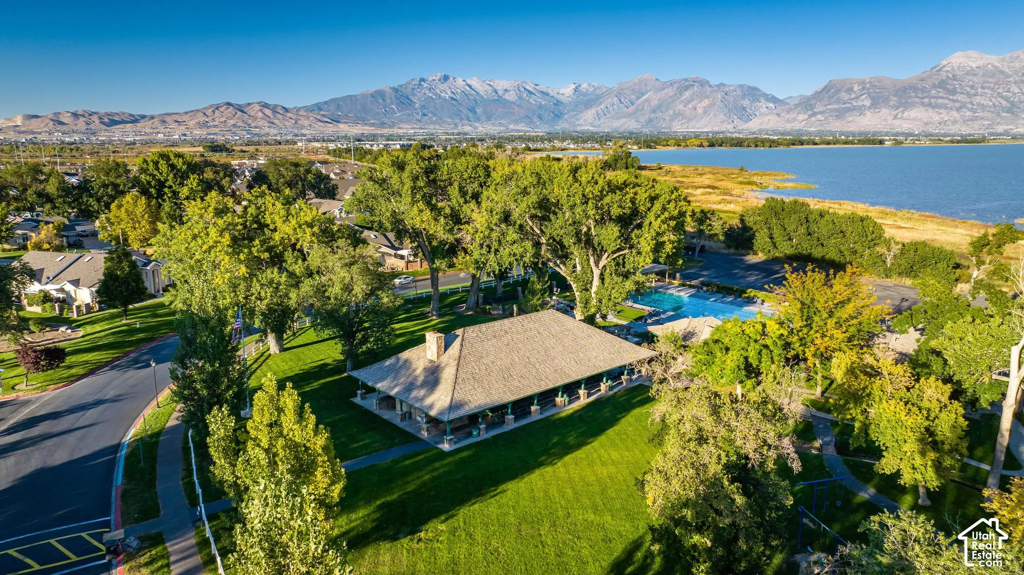 Aerial perspective featuring a large lake, distant mountains, mature trees, and a community building with an adjacent swimming pool