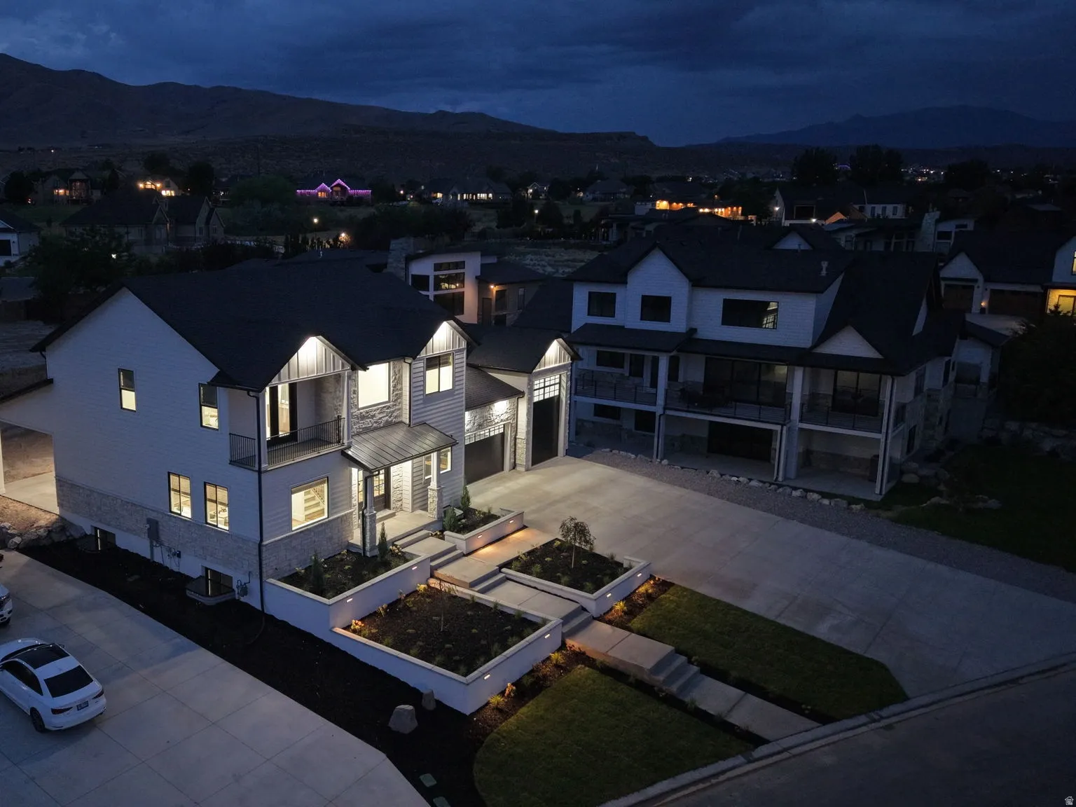 Modern exterior with stone and siding accents, illuminated landscaping, concrete driveway, and attached garage