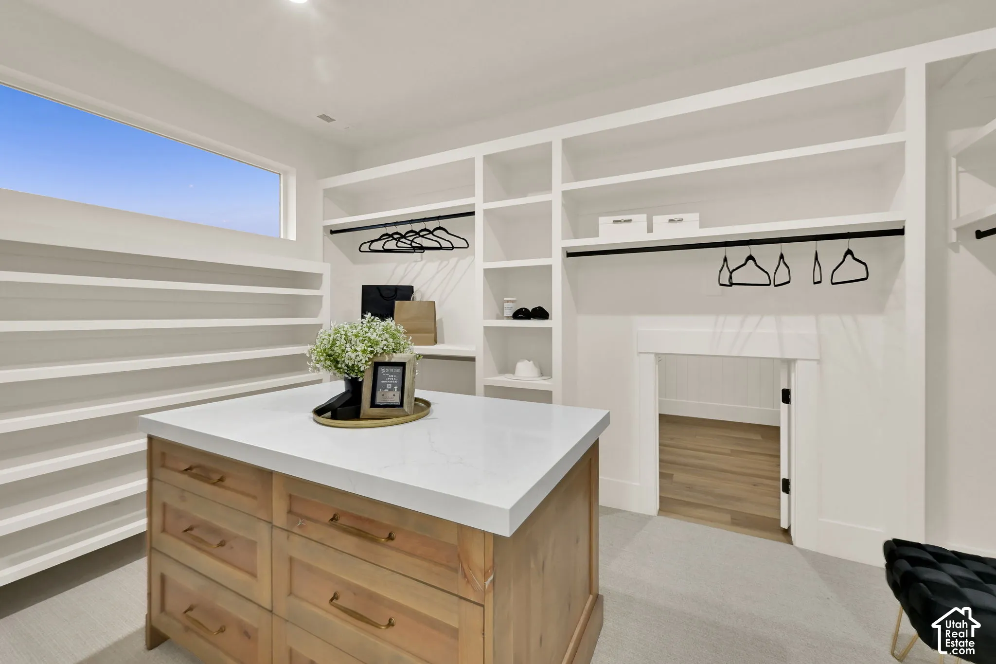 Custom built-in shelving, wood-finish center island with a light-toned countertop, integrated hanging rods, and a high horizontal window
