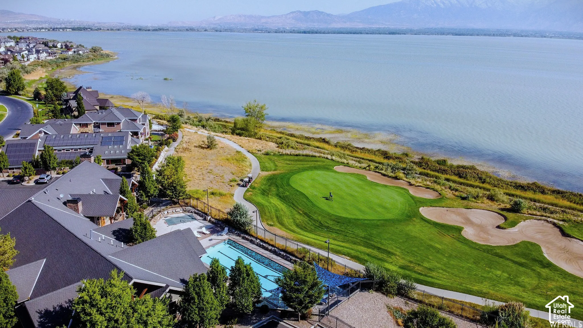Expansive lakefront setting with mountain backdrop, adjacent to a manicured golf course, and an outdoor swimming pool