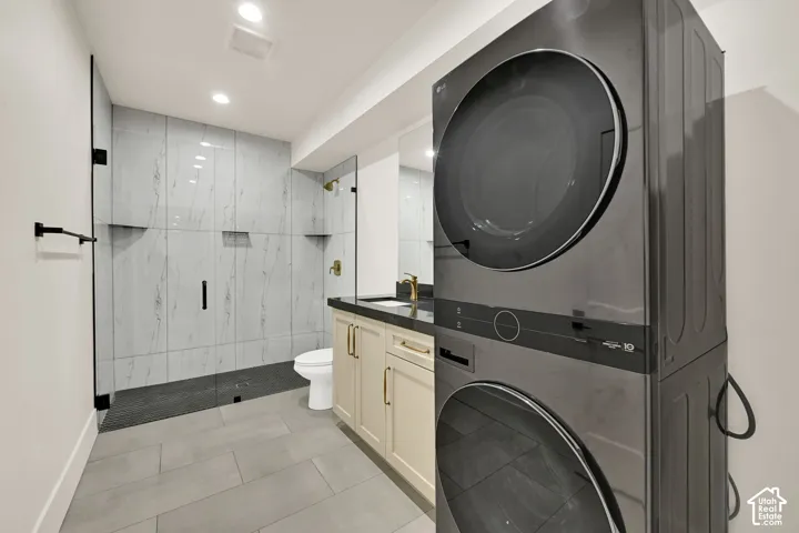 Built-in stacked washer and dryer, glass-enclosed shower with black fixtures, vanity with gold hardware, recessed lighting, and tile flooring