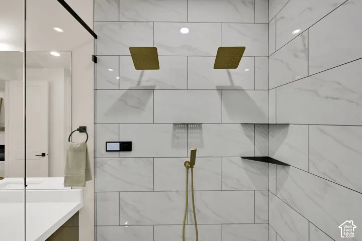 Spacious shower featuring dual brass rain showerheads, a hand-held shower fixture, and large-format tiled walls