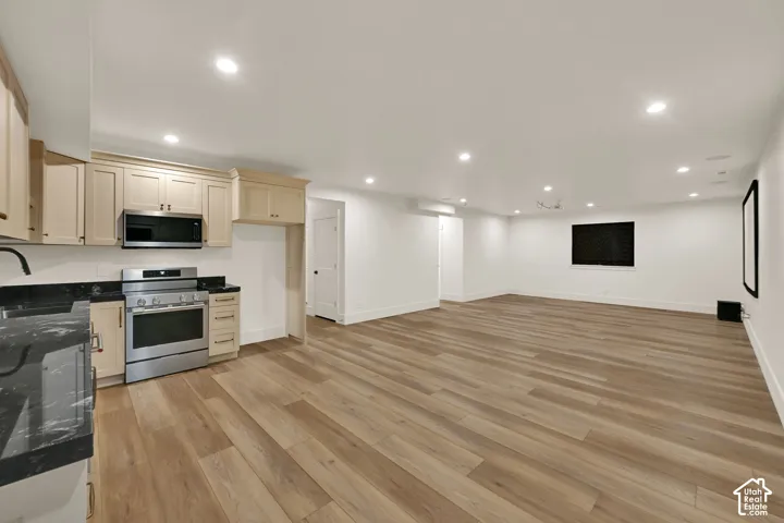 Spacious open-concept area featuring wood-finish flooring, a kitchen area with stainless steel appliances, dark countertops, and light-colored cabinetry