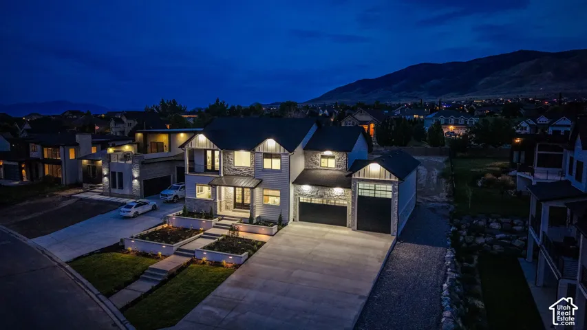 Stone and siding exterior with a multi-level concrete driveway, established landscaping with built-in planters, and an attached three-car garage