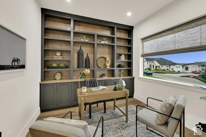 Built-in shelving with integrated cabinetry, wood-finish flooring, recessed lighting, and a large window with privacy shades