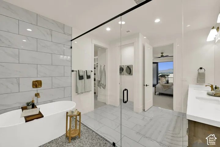 Freestanding soaking tub with a wall-mounted brass faucet, glass-enclosed shower, white tile flooring, and a double vanity with undermount sinks